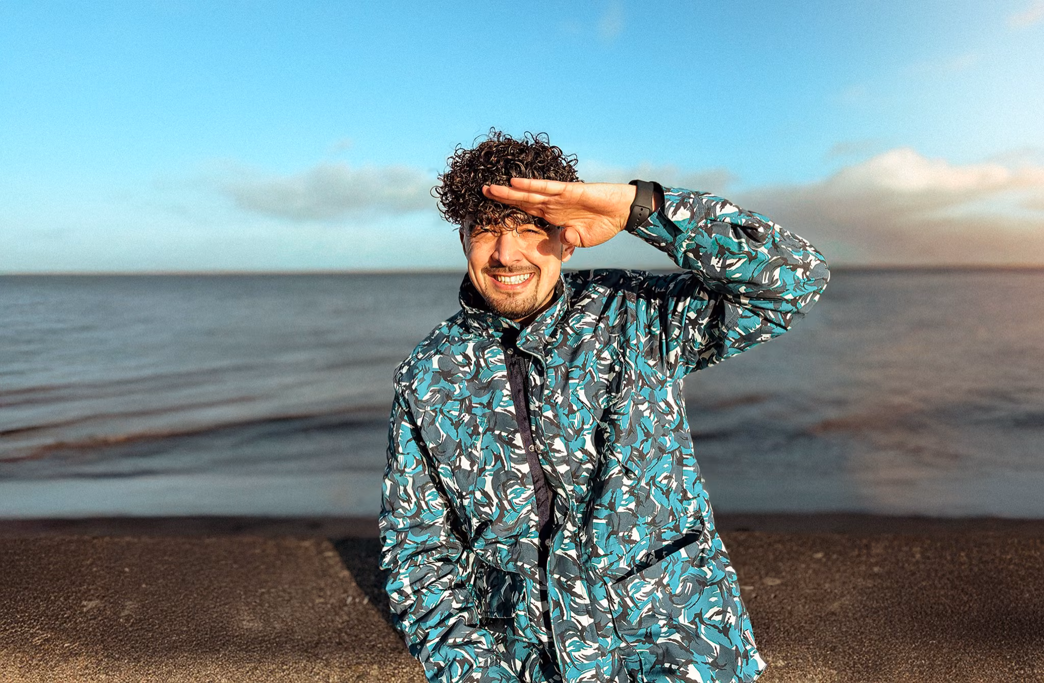 Gorka Di Capitan smiling by the sea in Scotland, shielding his eyes from the sun