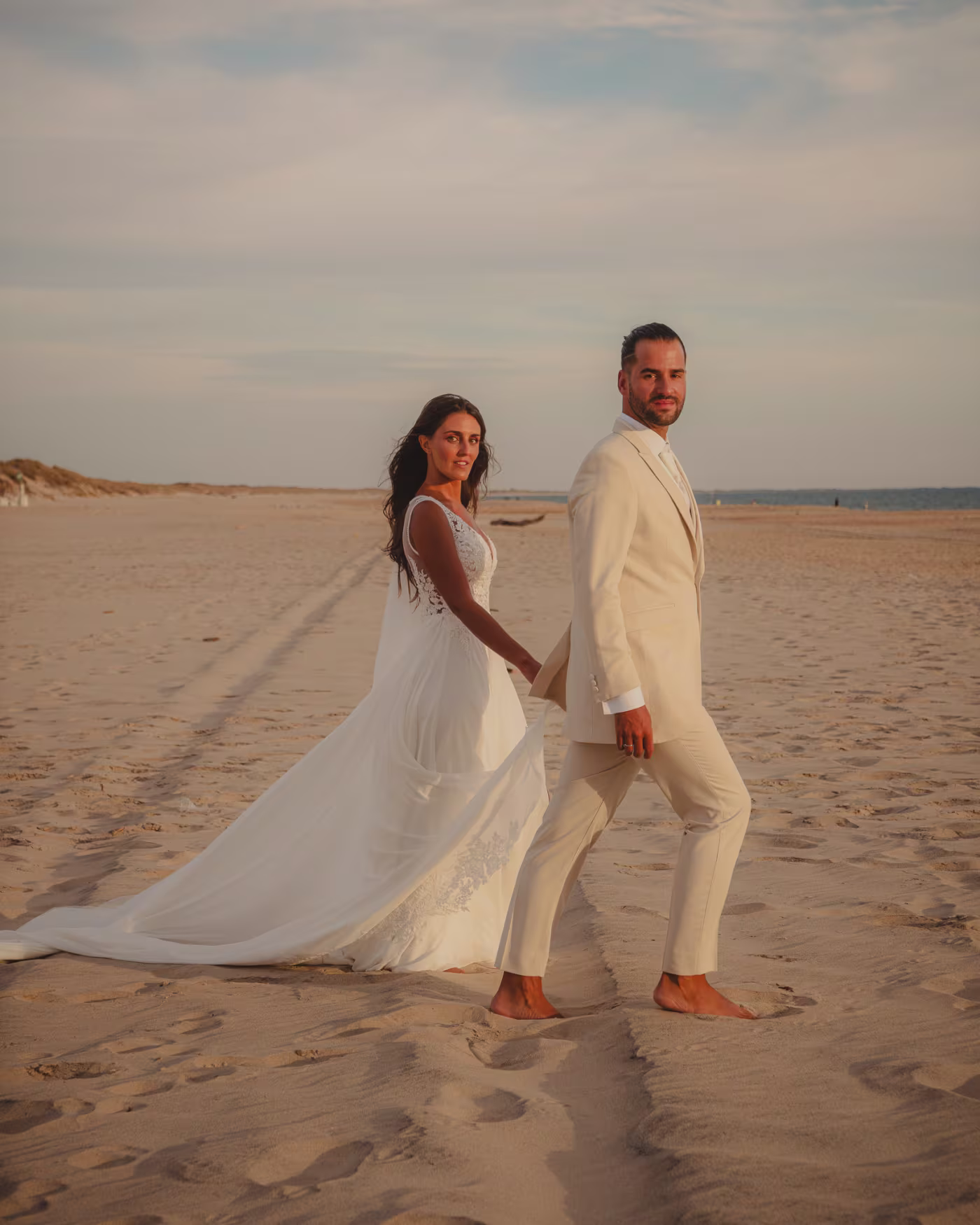 Bride and groom walking barefoot along the shore at golden hour in Huelva, Spain