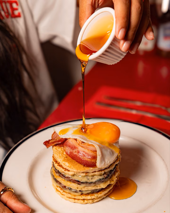 Maple syrup poured over a pancake stack with bacon and a fried egg at The City Cafe, Edinburgh