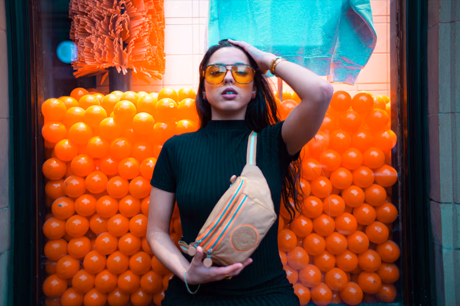 Model holding a Coronel Tapiocca bag against a wall of orange balloons, Glasgow