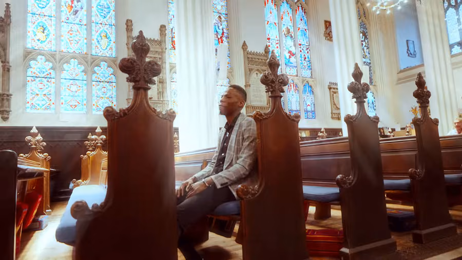 Kishaolin seated in the carved pews of a Scottish cathedral in the Lord Almighty music video
