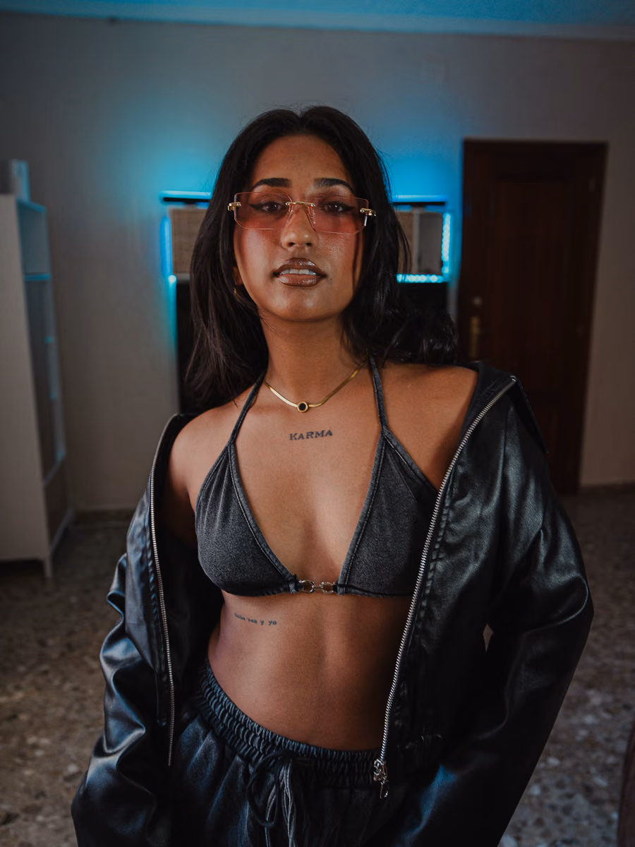 Maholas in an open leather jacket over a bikini top, lit by blue neon during a personal brand session in Valencia. Portrait photography by Gorka Di Capitan.