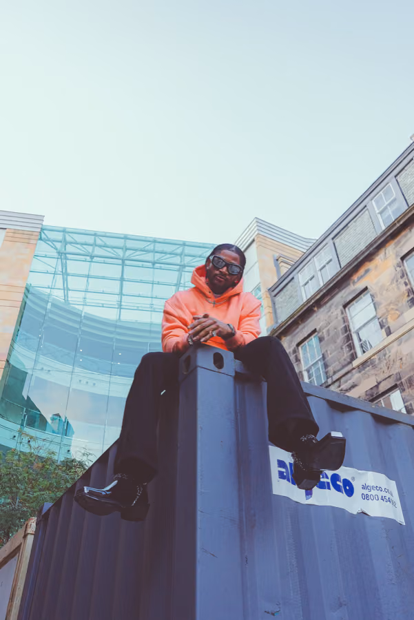 Model sitting on a shipping container wearing a Motivo Ink orange hoodie, Edinburgh