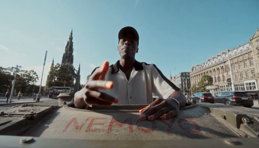 Kishaolin rising out of the hatch of a tank on Princes Street with NEMOYO painted in red on the hull and the Scott Monument behind, music video directed by Gorka Di Capitan